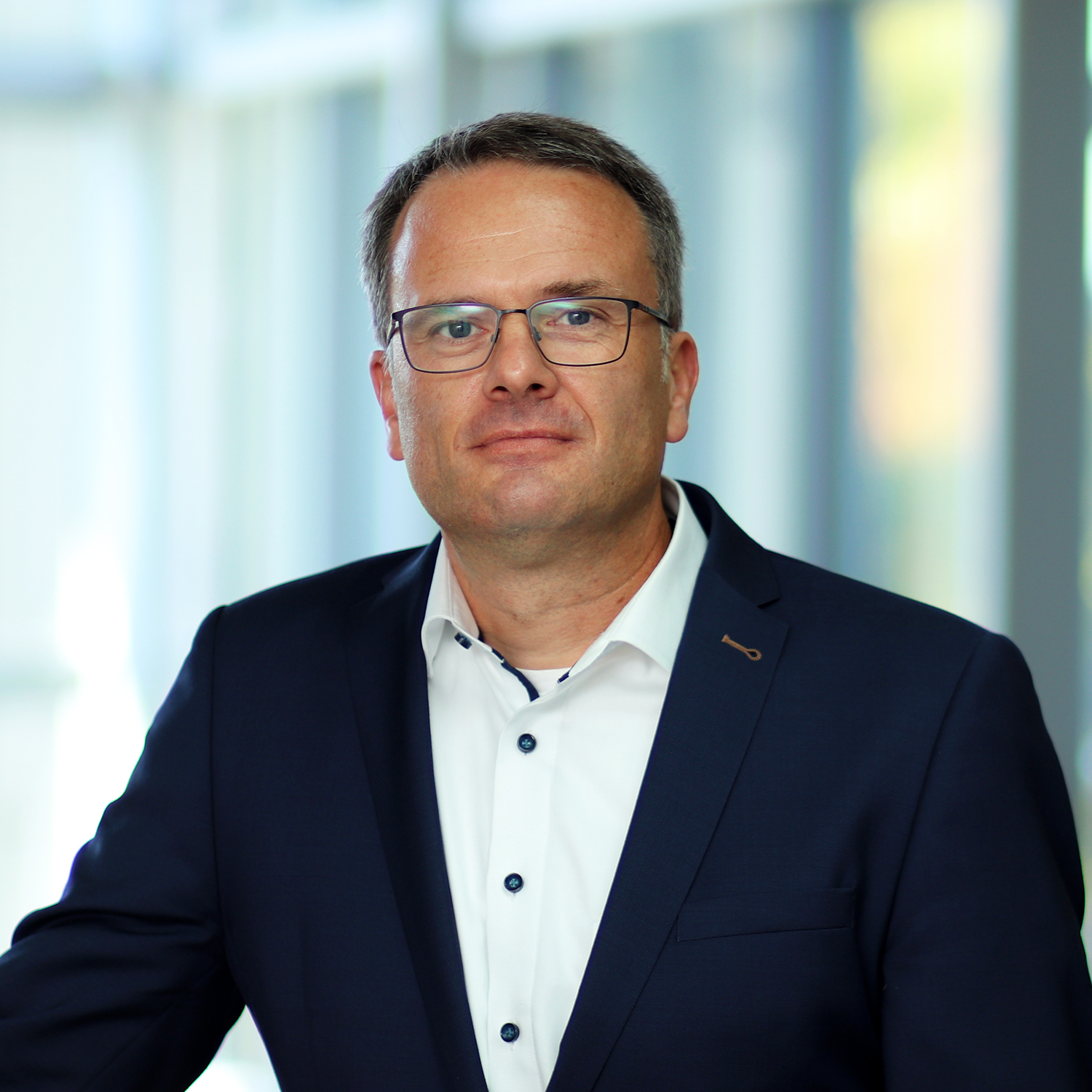 Ein Mann mit Brille trägt ein weißes Hemd und ein dunkles Jackett.