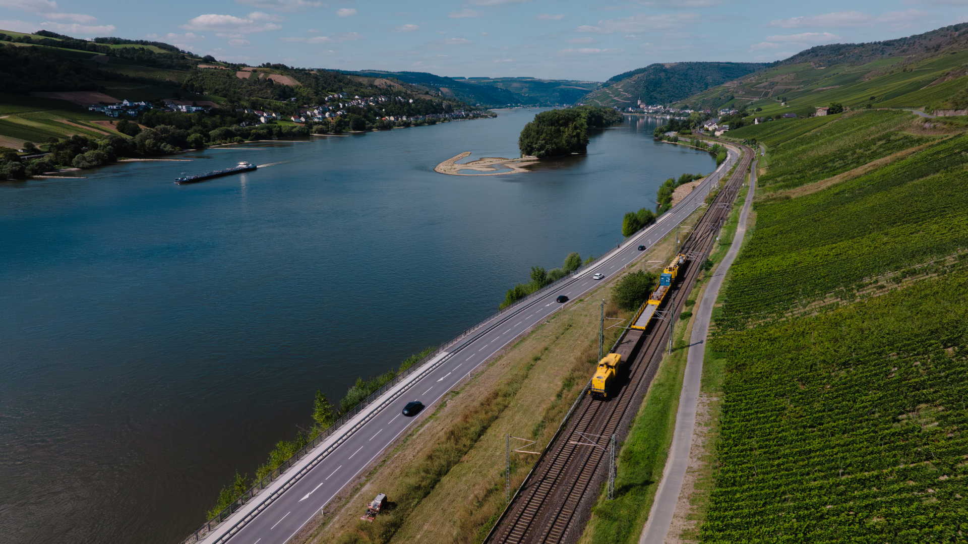 Ein Zug fährt entlang einer Gleisanlage neben einem Fluss.