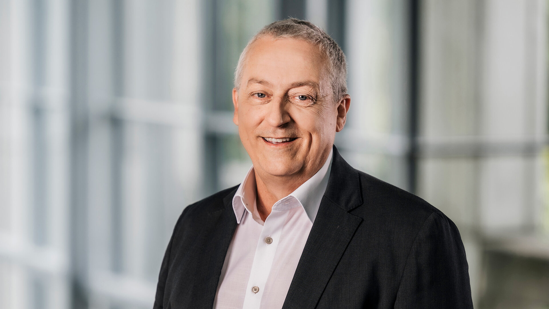 Foto von Ralf Schmidt, Ressortleiter Technik, stehend in Anzug und Hemd in einem modernen Bürogebäude.