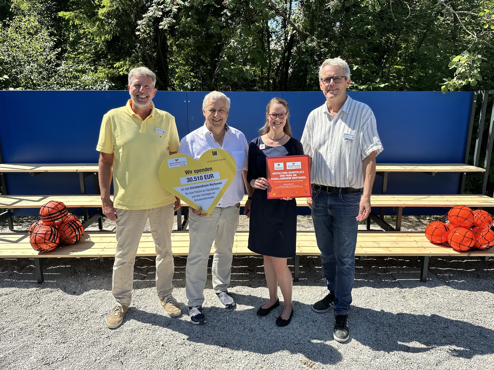 Drei Personen stehen vor einer Bank und halten ein Schild in den Händen.