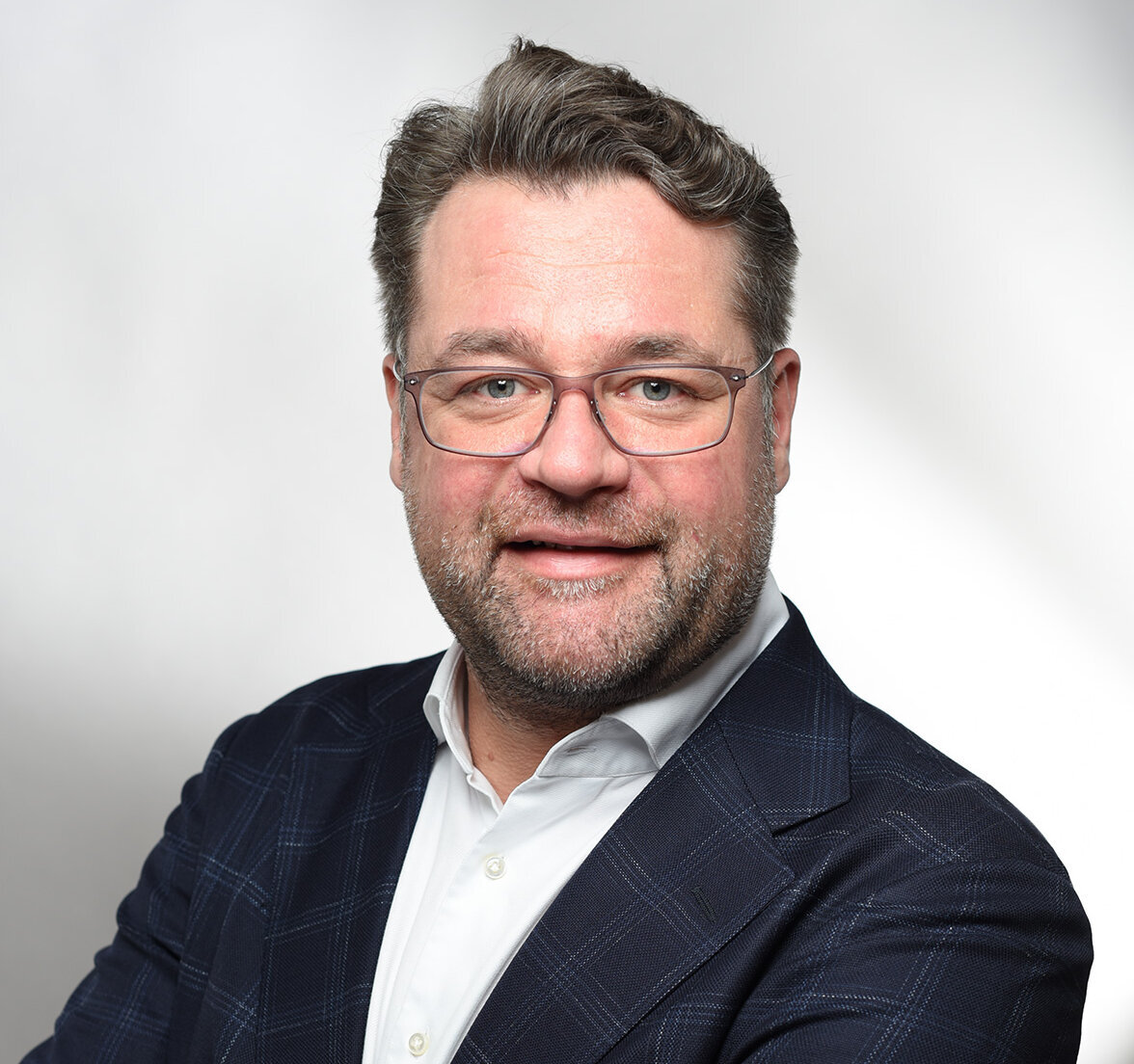Ein Mann mit Brille und Bart lächelt freundlich, während er seine Arme vor der Brust verschränkt.