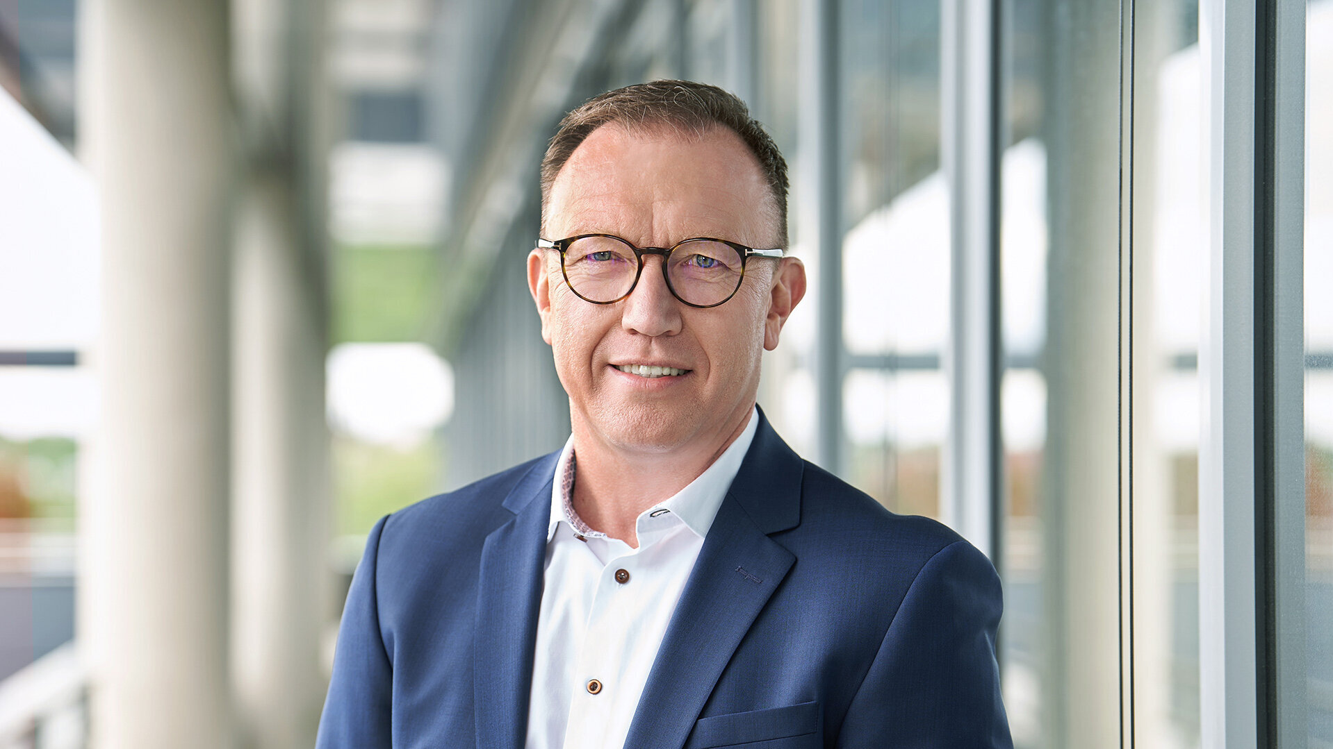 Photo of Marcus Herwarth, Head of Track Infrastructure Construction and Chairman of the Management Board, standing in a suit and shirt in front of a modern office building.