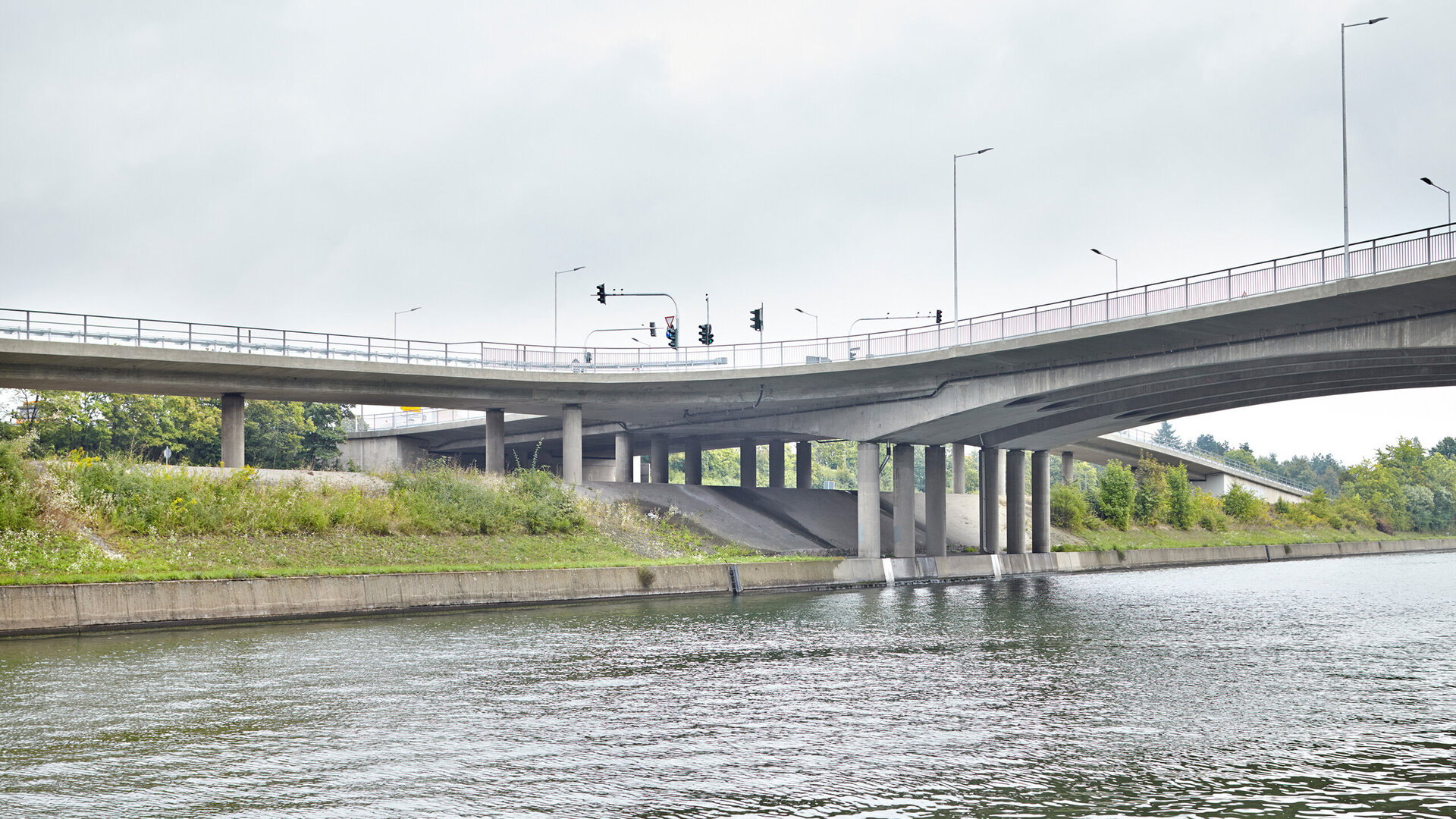 Ein Blick auf eine Brücke, die über einen Fluss führt, mit Verkehrssignalen und einer bewachsenen Uferlinie im Hintergrund.