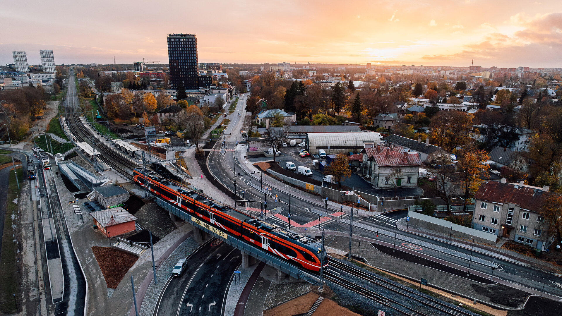 Ein Zug überquert die Kreuzung Tondi in einer urbanen Umgebung, während die Stadt Talinn im goldenen Licht der Dämmerung erstrahlt.
