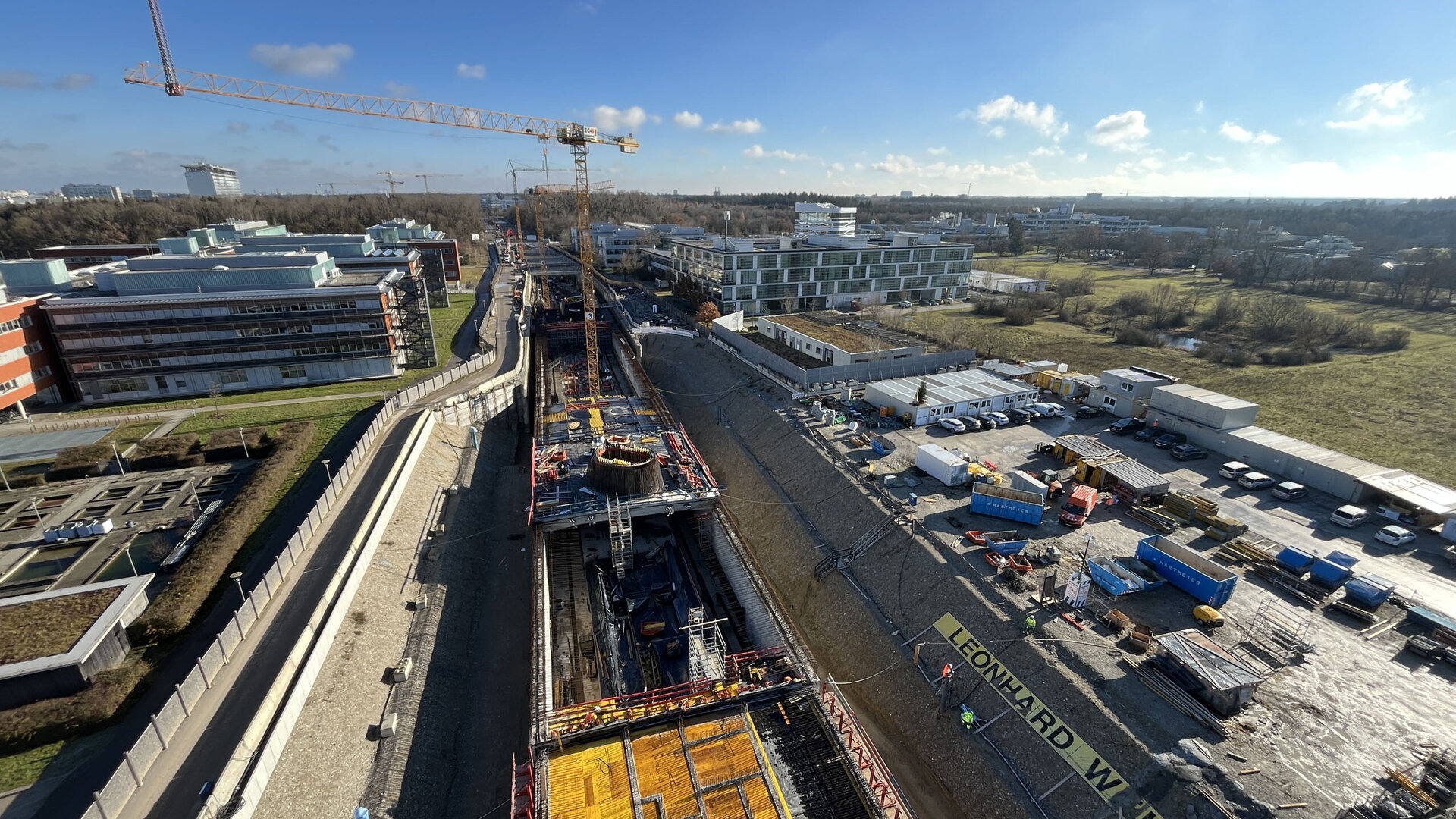 Blick auf eine große Baustelle mit einem Kran, der über ein Bauprojekt schwebt, während Fahrzeuge und Materialien in der Nähe stehen.