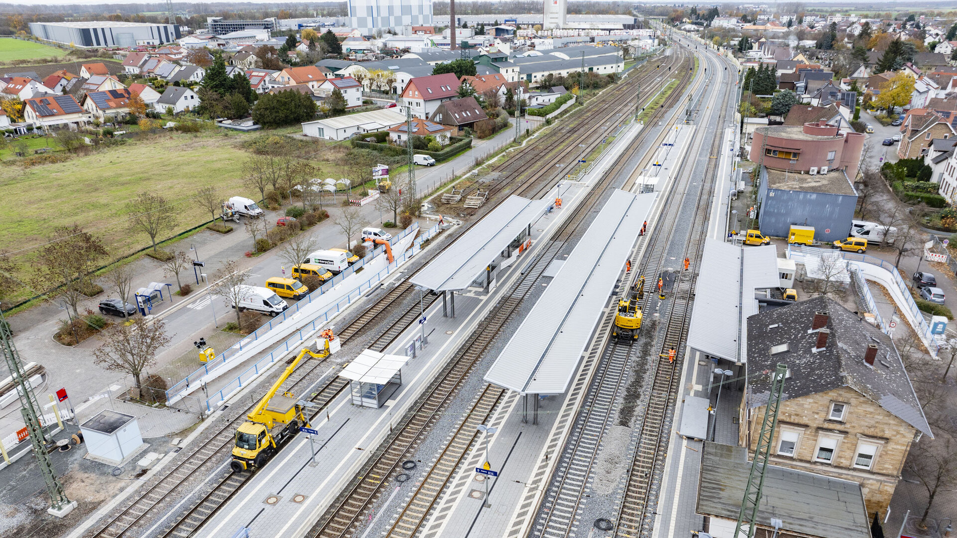 Ein Bahnhof im Umbau, mit mehreren Arbeitern, die an den Gleisen arbeiten, und gelben Fahrzeugen, die die Baustelle unterstützen.