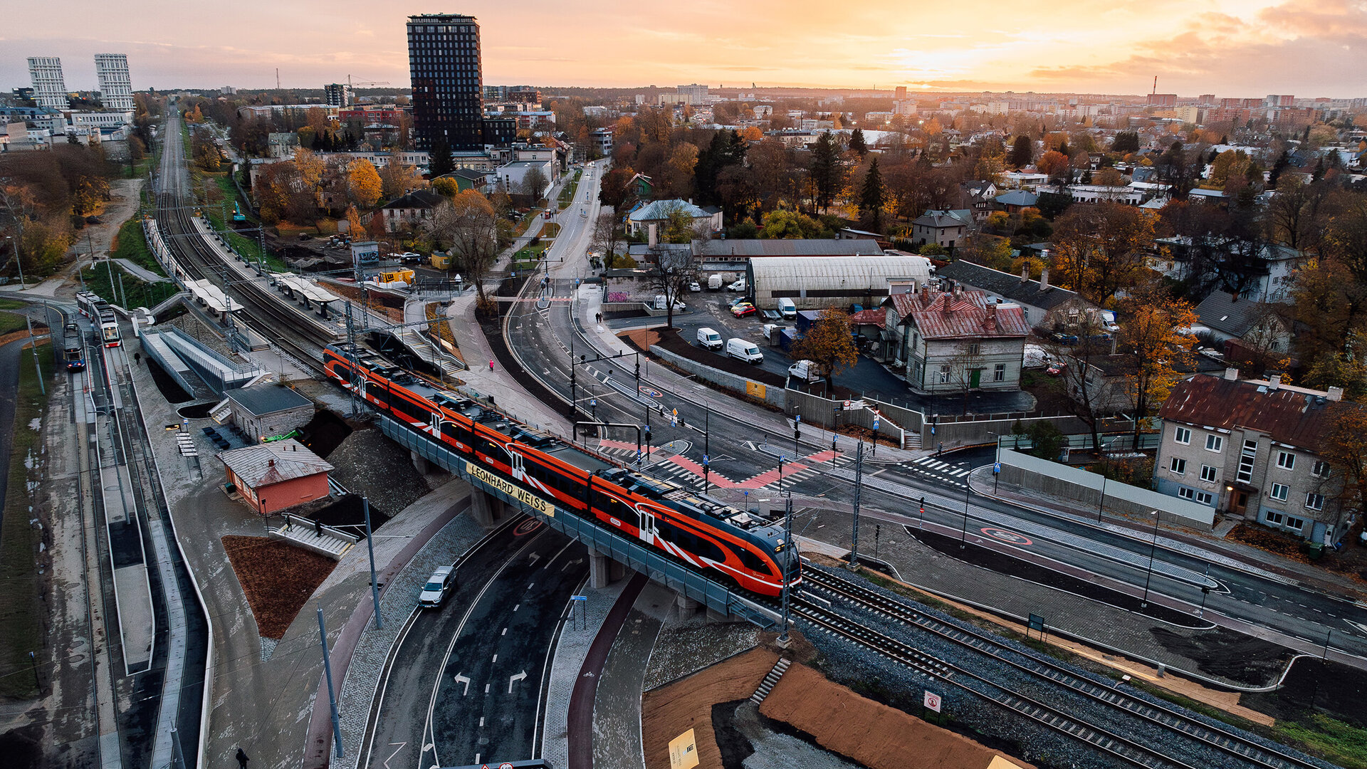 Ein Zug überquert die Kreuzung Tondi in einer urbanen Umgebung, während die Stadt Talinn im goldenen Licht der Dämmerung erstrahlt.
