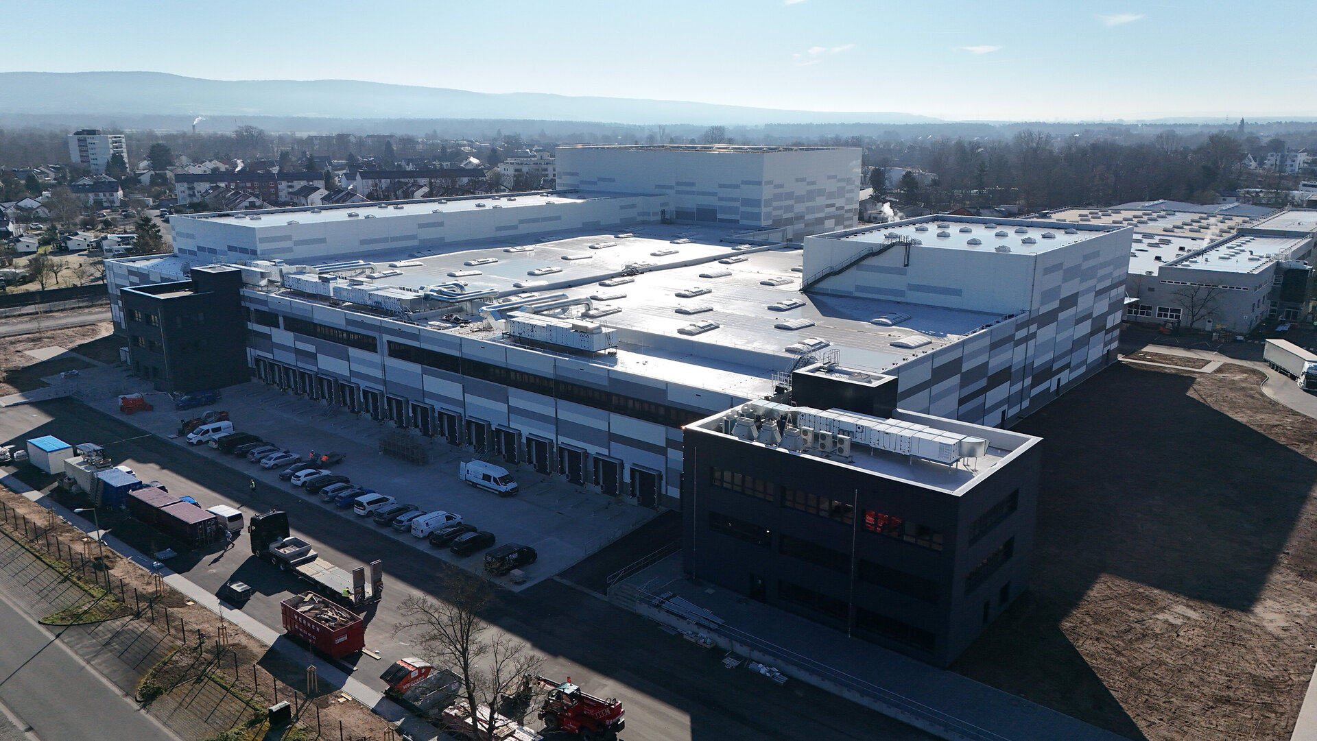 Ein modernes Industriegebäude mit einem großen Flachdach und mehreren Lüftungsanlagen, umgeben von einem Parkplatz.