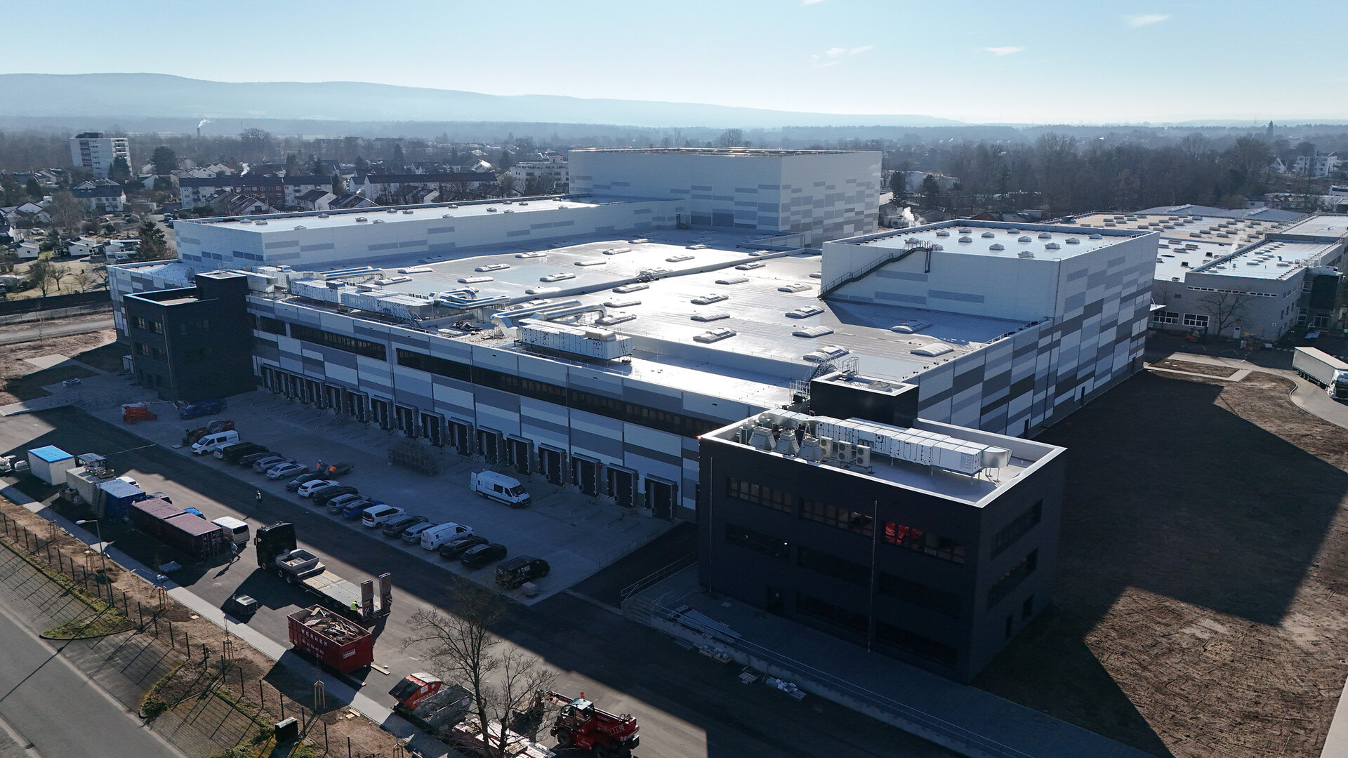 Ein modernes Industriegebäude mit einem großen Flachdach und mehreren Lüftungsanlagen, umgeben von einem Parkplatz.