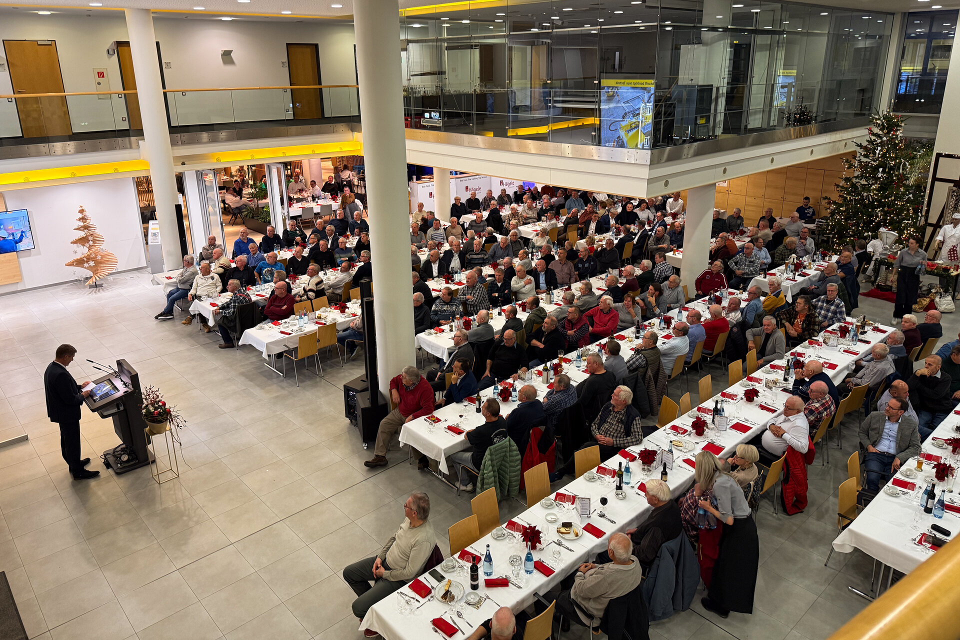 Eine große Gruppe von Menschen sitzt an Tischen in einem geräumigen Raum.
