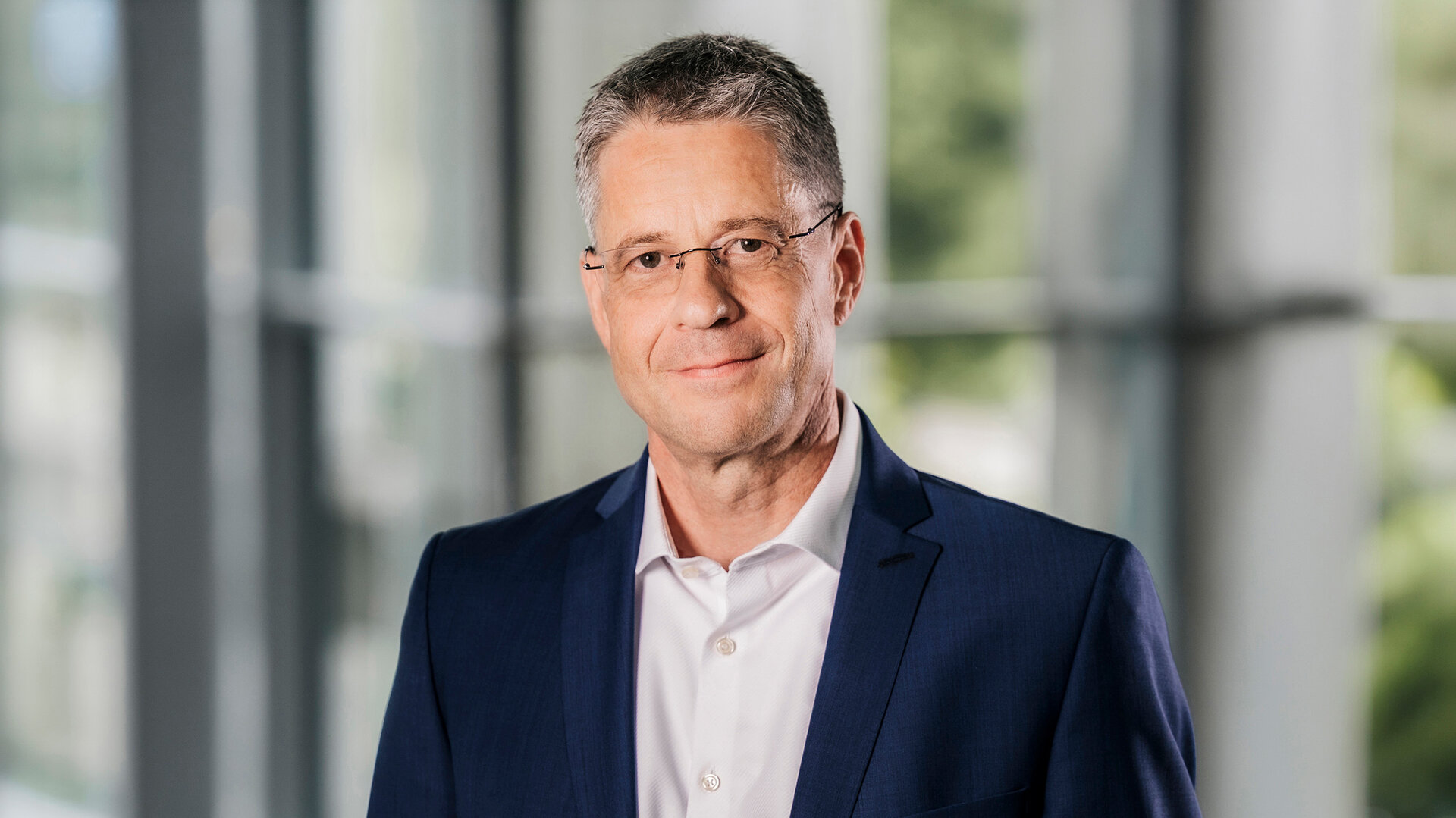 Foto von Steffen Schönfeld, Ressortleiter Ingenieur- und Schlüsselfertigbau, stehend in Anzug und Hemd in einem modernen Bürogebäude.