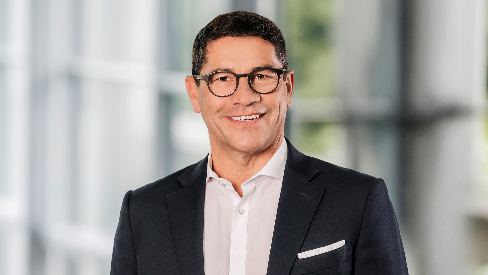 Foto von Stefan Schmidt-Weiss, Ressortleiter Ressourcen und Beteiligungen, stehend in Anzug und Hemd in einem modernen Bürogebäude.