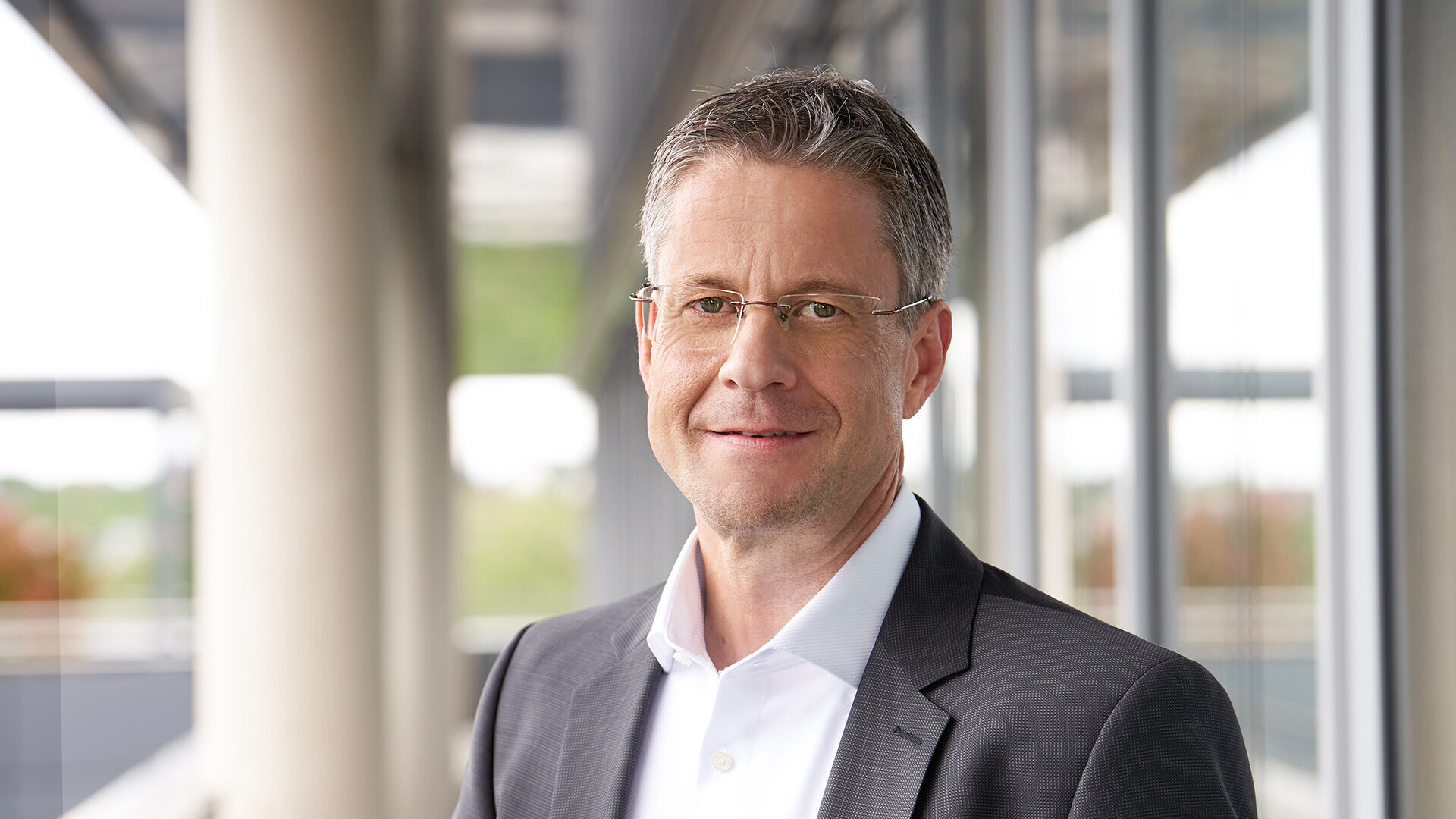 Photo of Steffen Schönfeld, Head of Engineering and Turnkey Construction, standing in a suit and shirt in front of a modern office building.