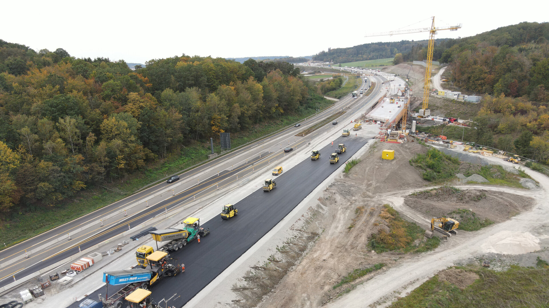Eine Baustelle an einer Autobahn mit mehreren Baumaschinen, die Asphalt auftragen und eine neue Fahrbahn erstellen.