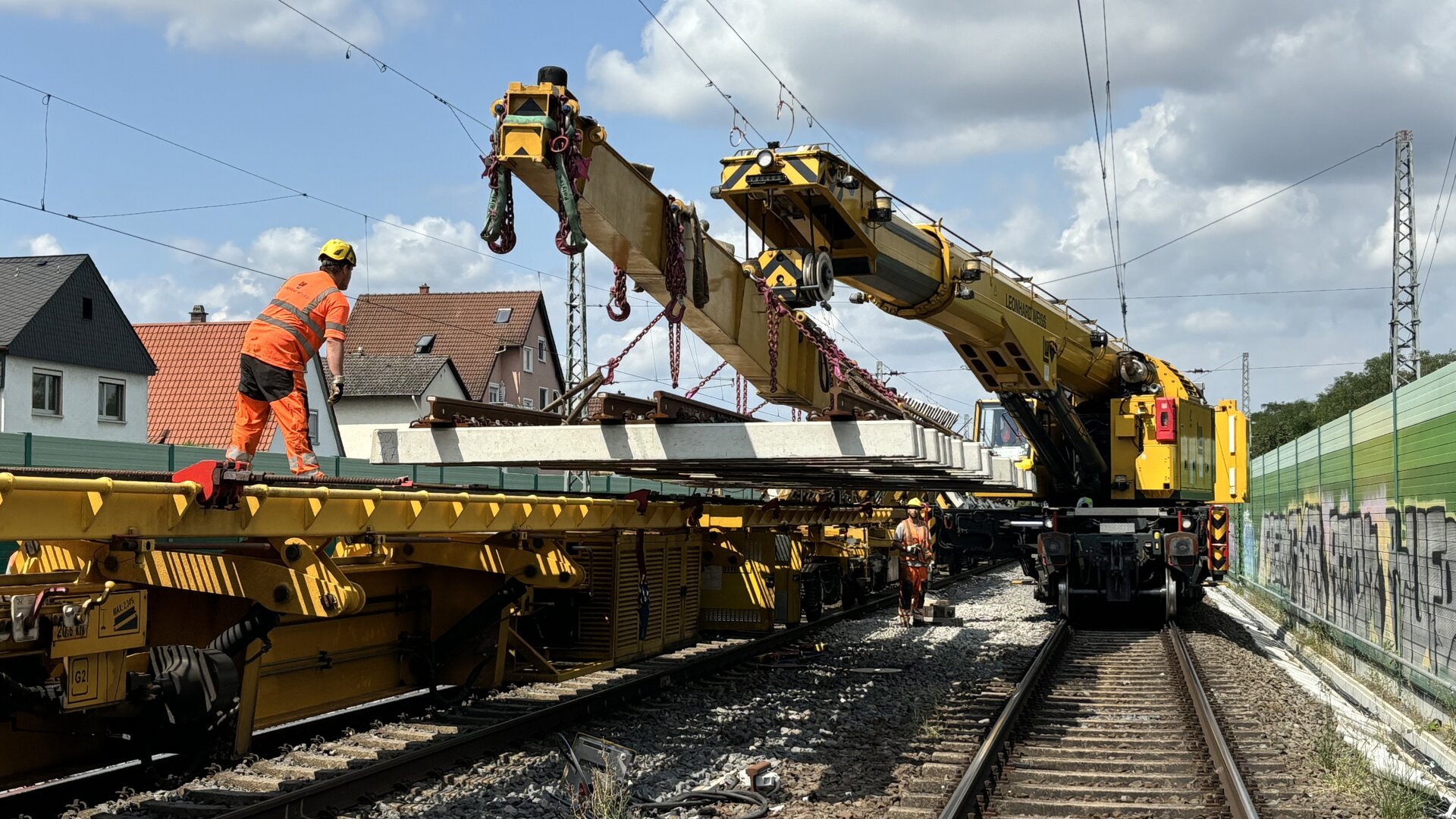 Arbeiter in orangefarbener Sicherheitskleidung beim Weicheneinbau mittels Weichentransportwagen und Eisenbahndrehkran.