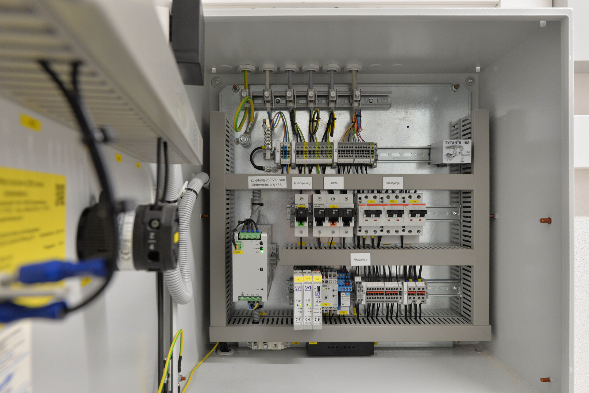 Offener Schaltschrank mit zahlreichen Kabeln, Sicherungen, Schaltern und elektronischen Bauteilen. Die Leitungen sind sauber geordnet und beschriftet, sichtbar sind unter anderem Anschlüsse für AC-Einspeisung, Batterien und DC-Kopplung. Industrielle Elektroinstallation.