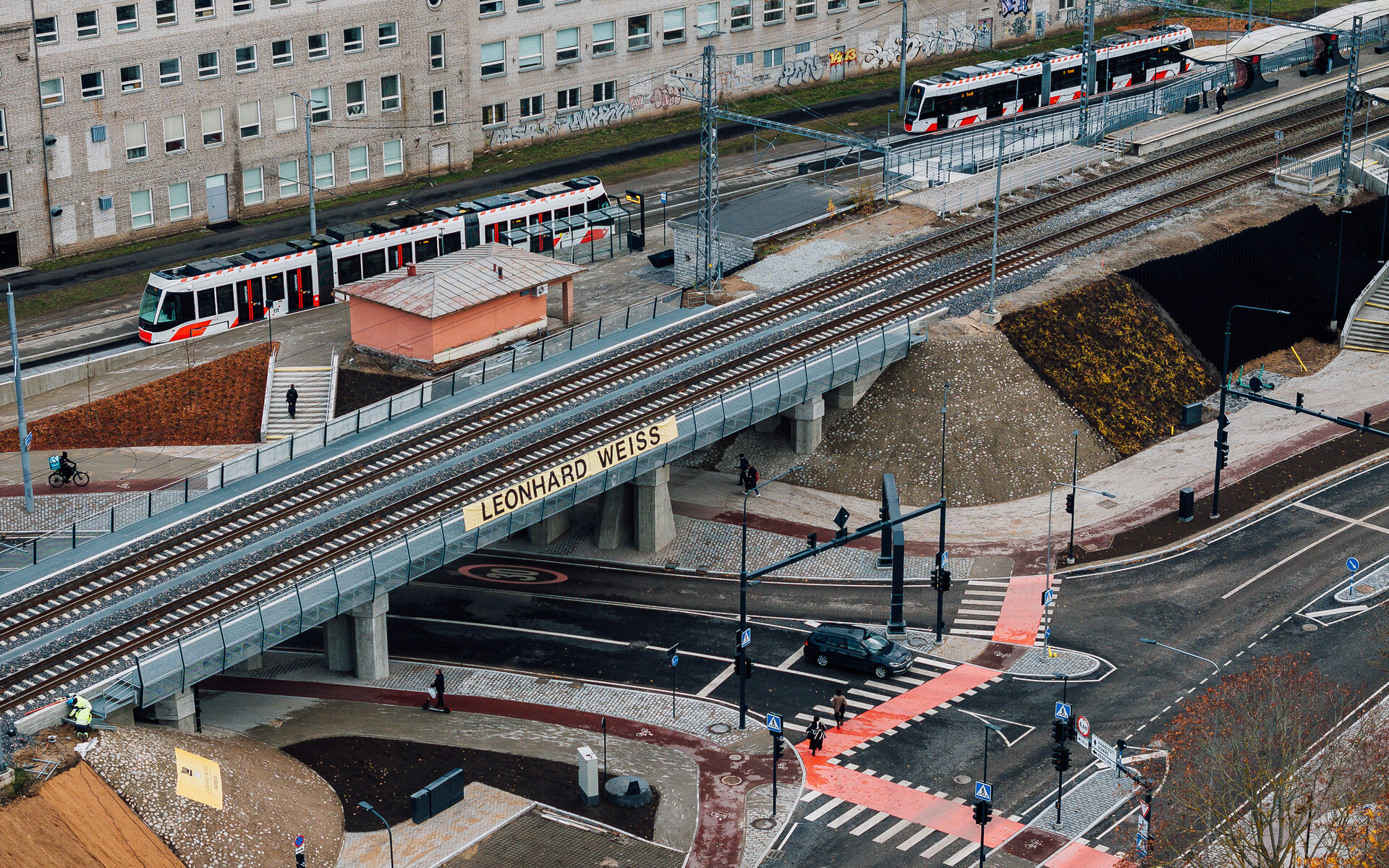 Eine Straßenbahn fährt über den Tondi-Viadukt, während Fußgänger und Radfahrer die Straße darunter überqueren.