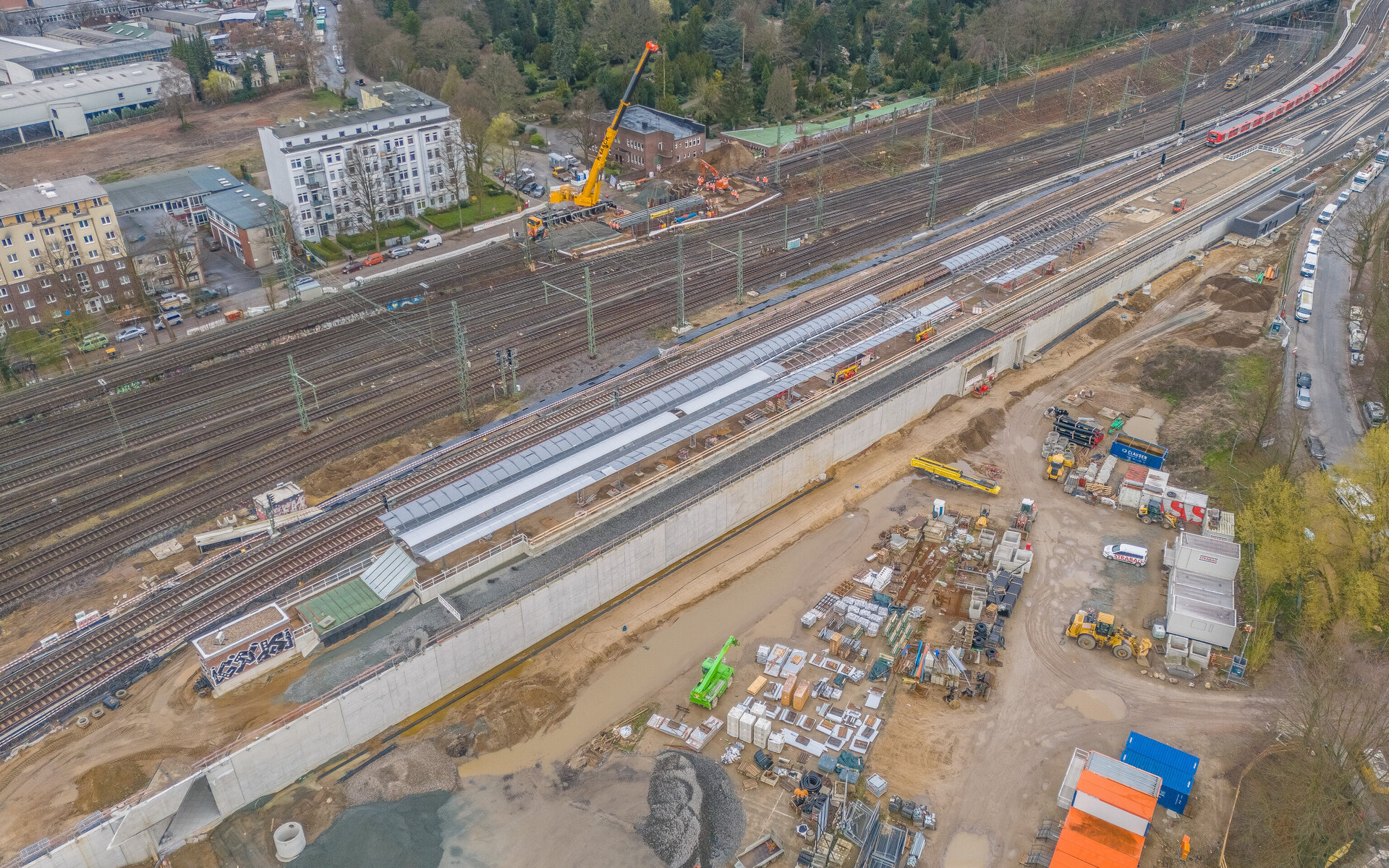 Blick auf eine umfangreiche Bahnbaustelle mit Gleisen, einem Kran und verschiedenen Baustellenfahrzeugen im Vordergrund.