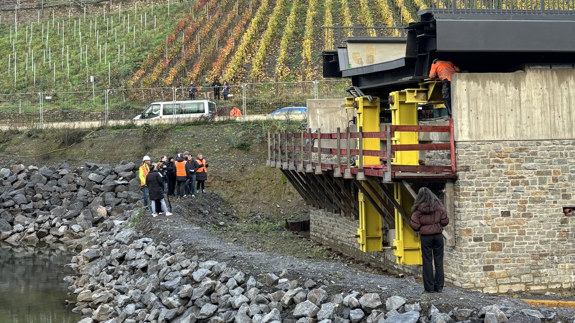 Eine Gruppe von Menschen in orangefarbenen Westen steht am Ufer der Ahr  und betrachtet den Brückeneinschub zwischen der Felspartie „Bunte Kuh“ und Marienthal.