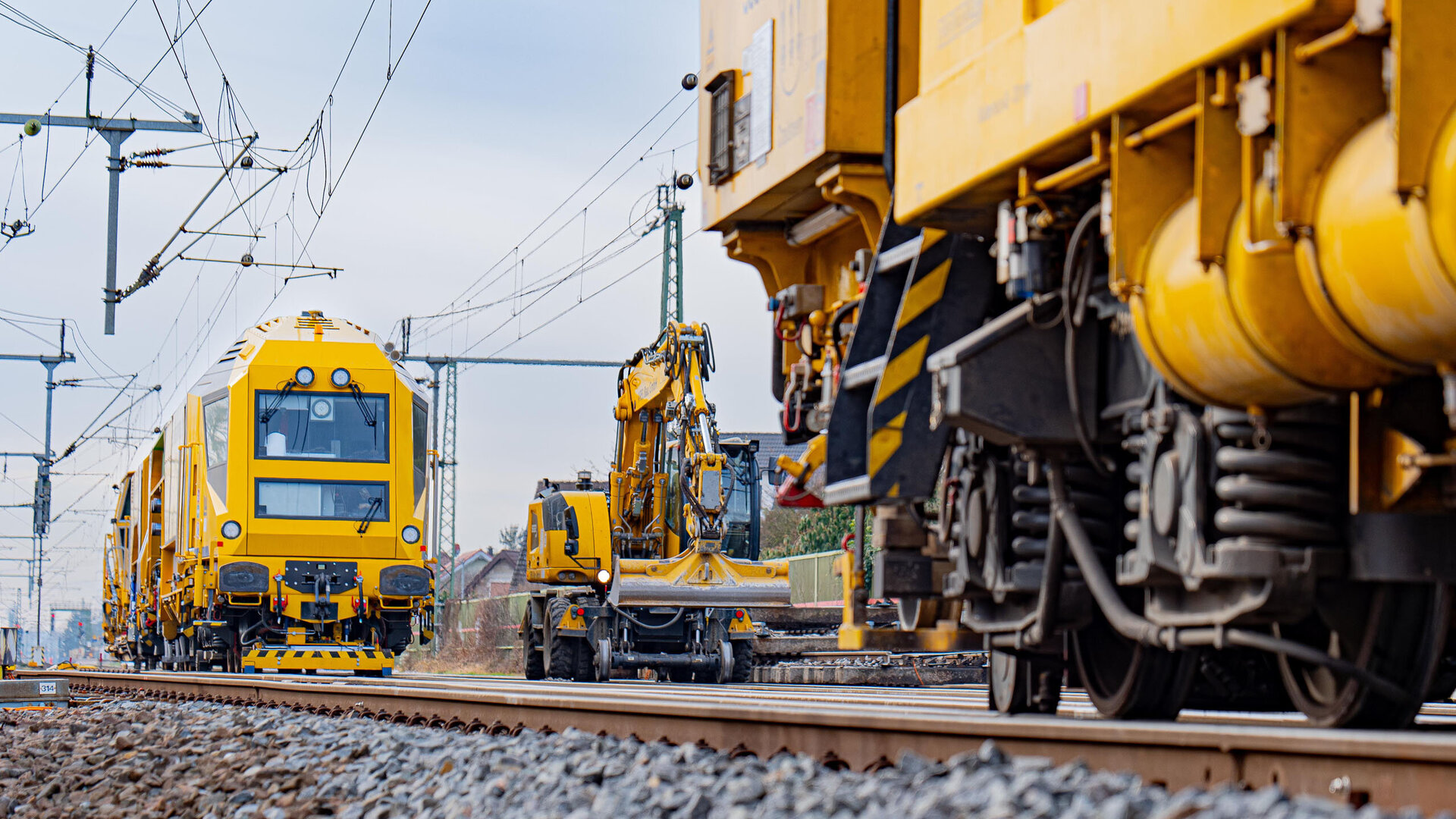 Ein gelbes Gleisbaufahrzeug fährt auf den Schienen, während ein weiterer Bagger in der Nähe mit der Gleisarbeit beschäftigt ist.
