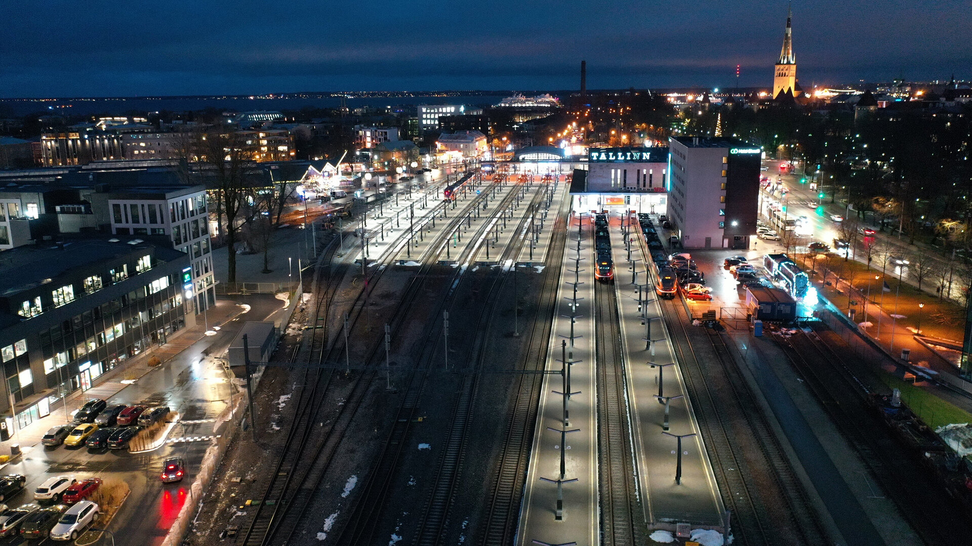 Eine nächtliche Ansicht des Bahnhofs in Tallinn, beleuchtet von Straßenlaternen und umgeben von modernen Gebäuden.