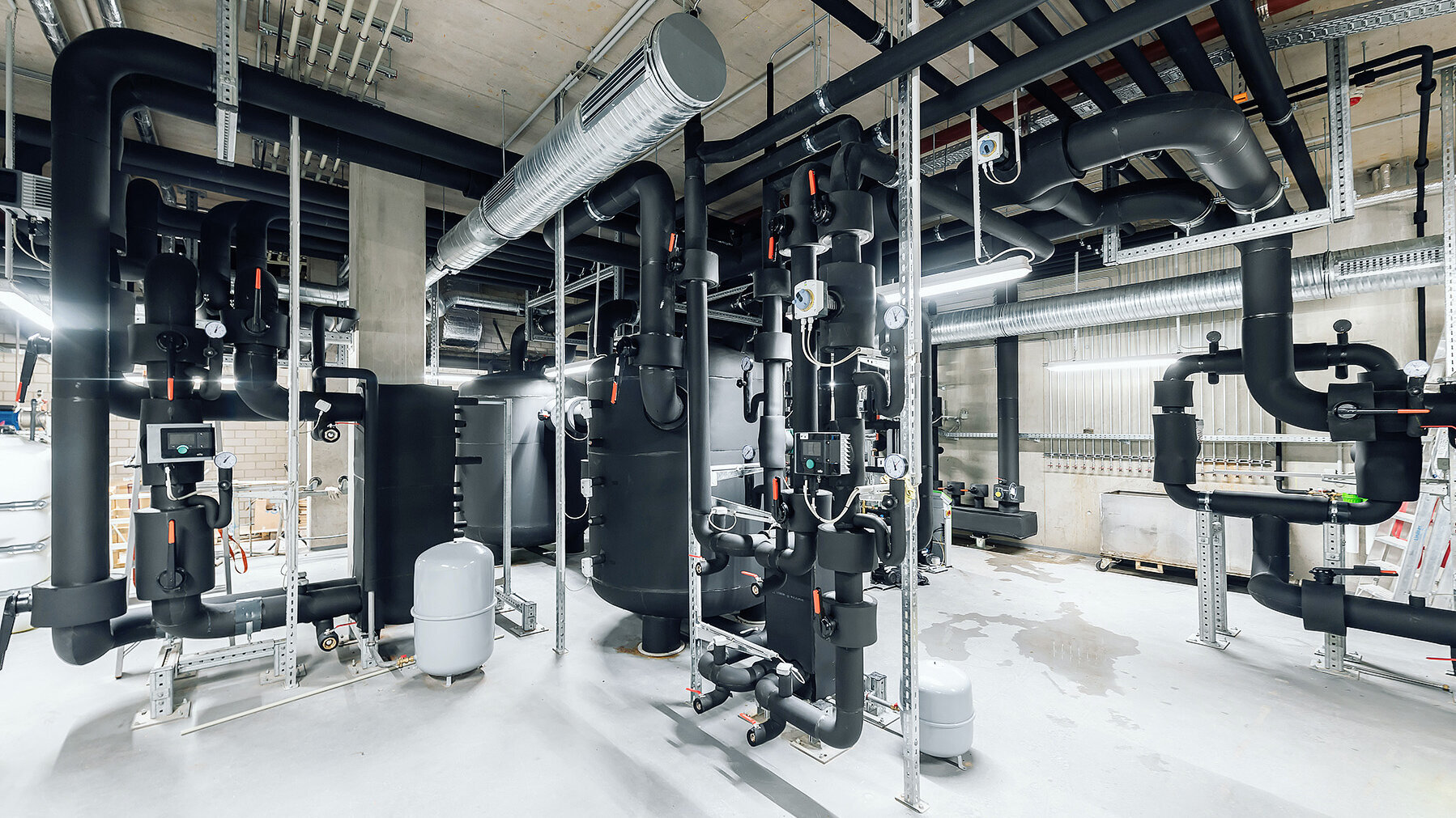 Ein komplexes Rohrleitungssystem mit schwarzen Rohren und verschiedenen Messgeräten in einem modernen Technikraum.