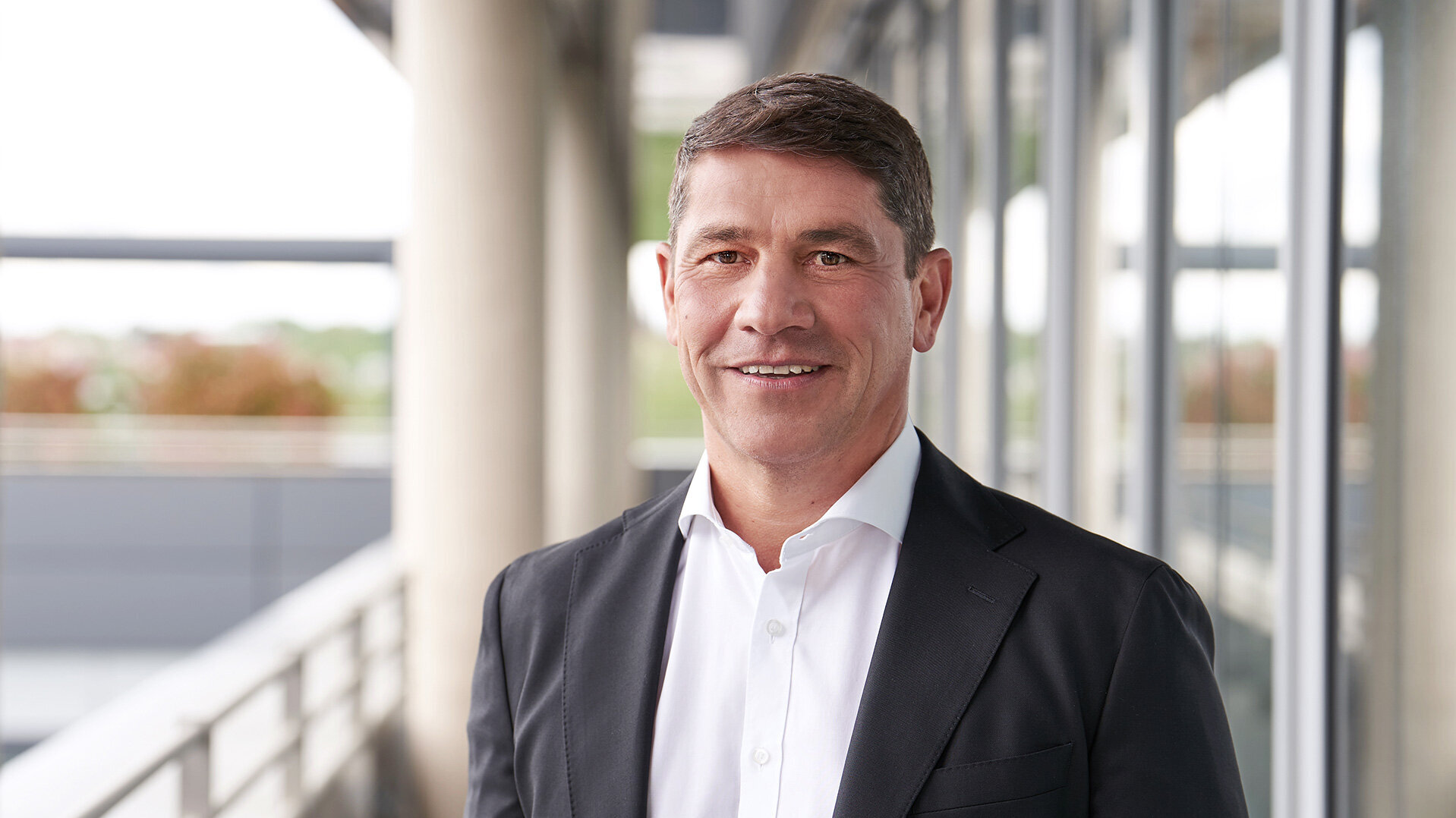 Photo of Stefan Schmidt-Weiss, Head of Resources and Investments, standing in a suit and shirt in front of a modern office building.
