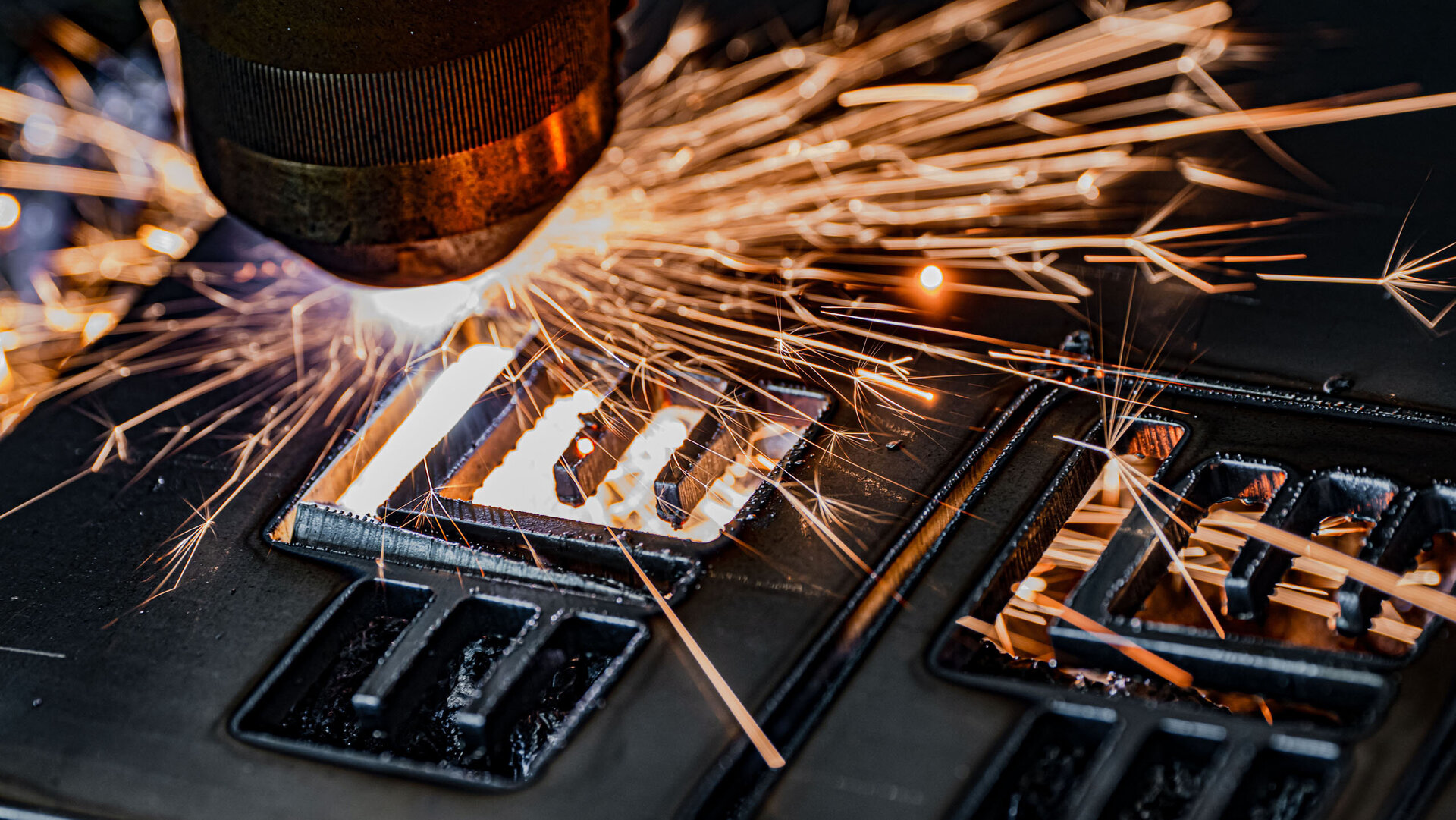 Intensive Funken fliegen von einer Metalloberfläche, während ein Laserstrahl präzise Formen in das Material schneidet.