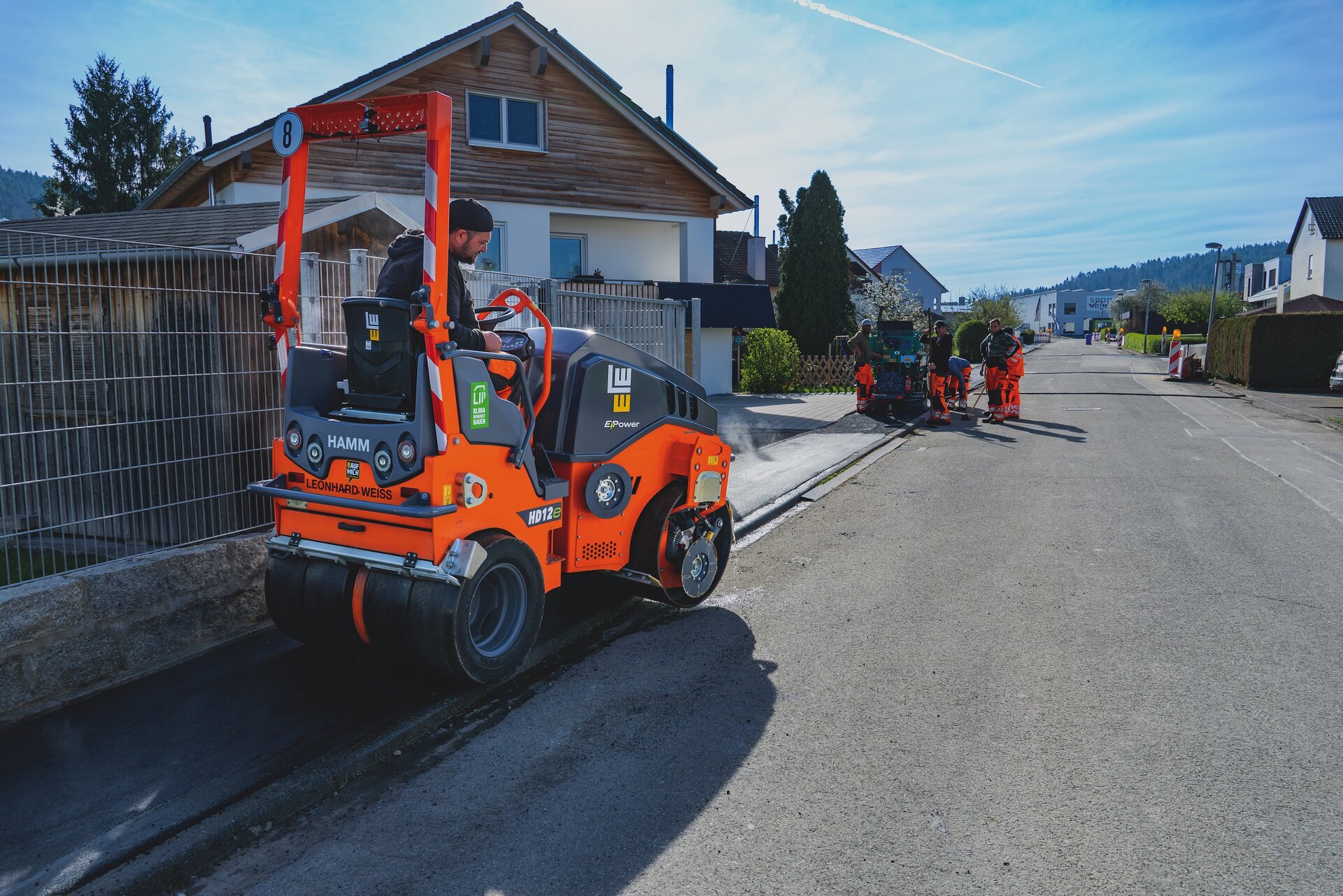 Ein Baustellenmitarbeiter sitzt auf einer Elektro Asphaltwalze.