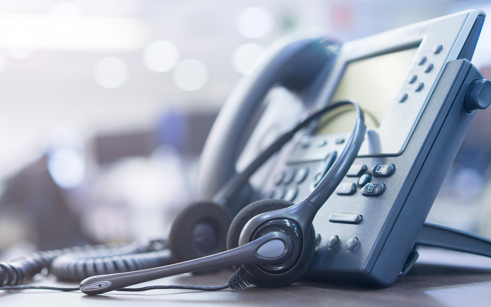 Auf dem Tisch liegt ein Telefon mit einem Headset, umgeben von einem hellen, modernen Büro, das zur Kommunikation einlädt.