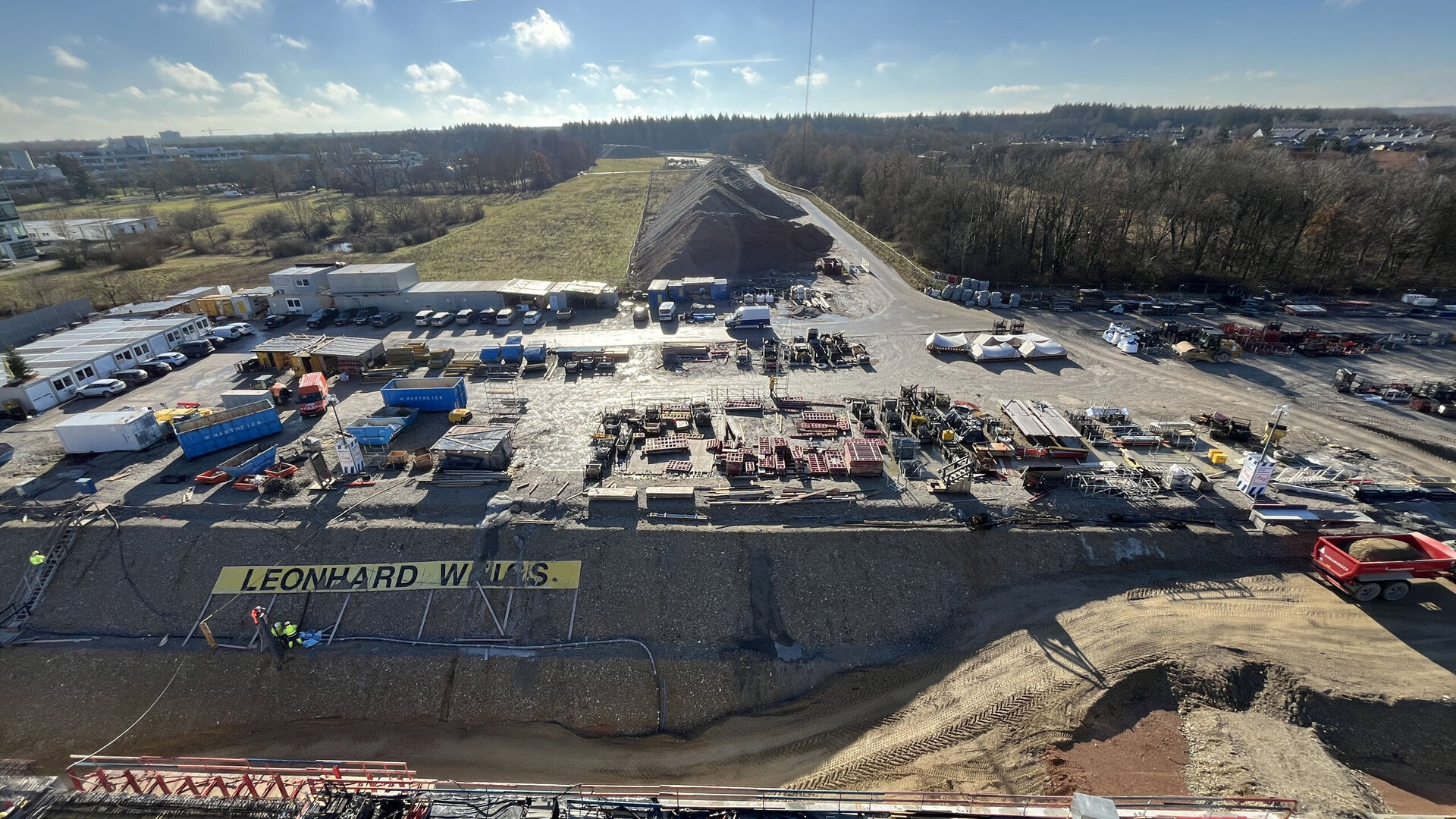 Ein Blick auf eine große Baustelle mit verschiedenen Baustellenfahrzeugen und einem klaren, sonnigen Himmel darüber.