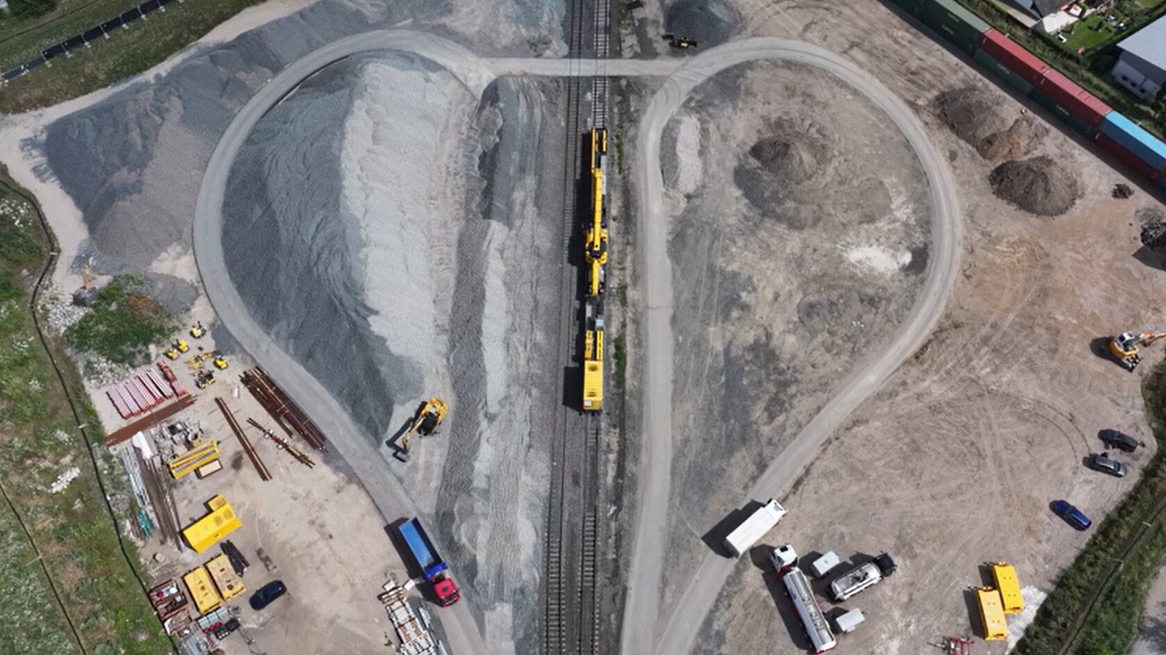 Eine Luftaufnahme zeigt eine Baustelle mit Schotterhaufen und Baumaschinen, die an den Gleisen arbeiten.