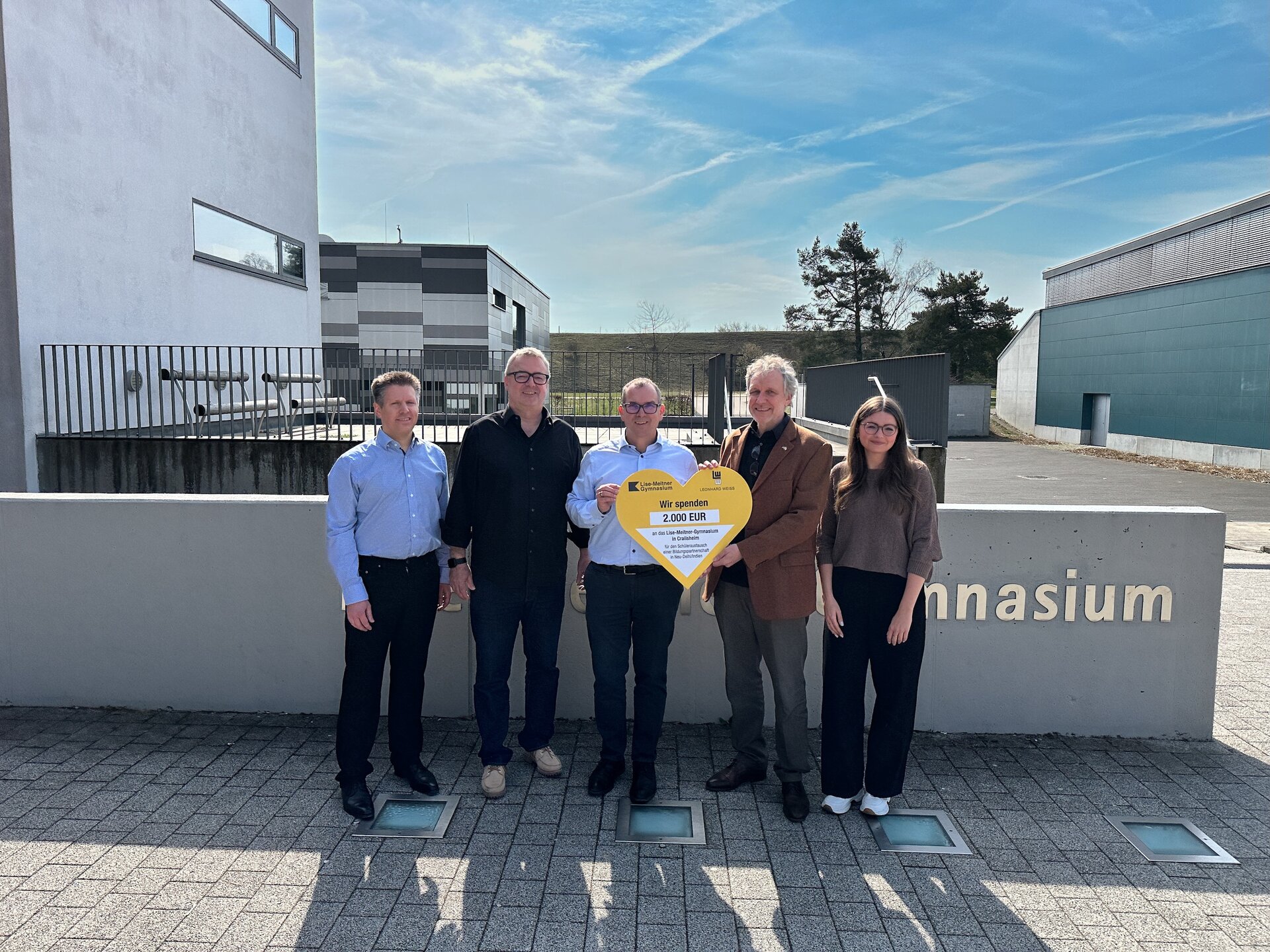 Fünf Personen halten einen Spendenscheck in Herzform hoch.