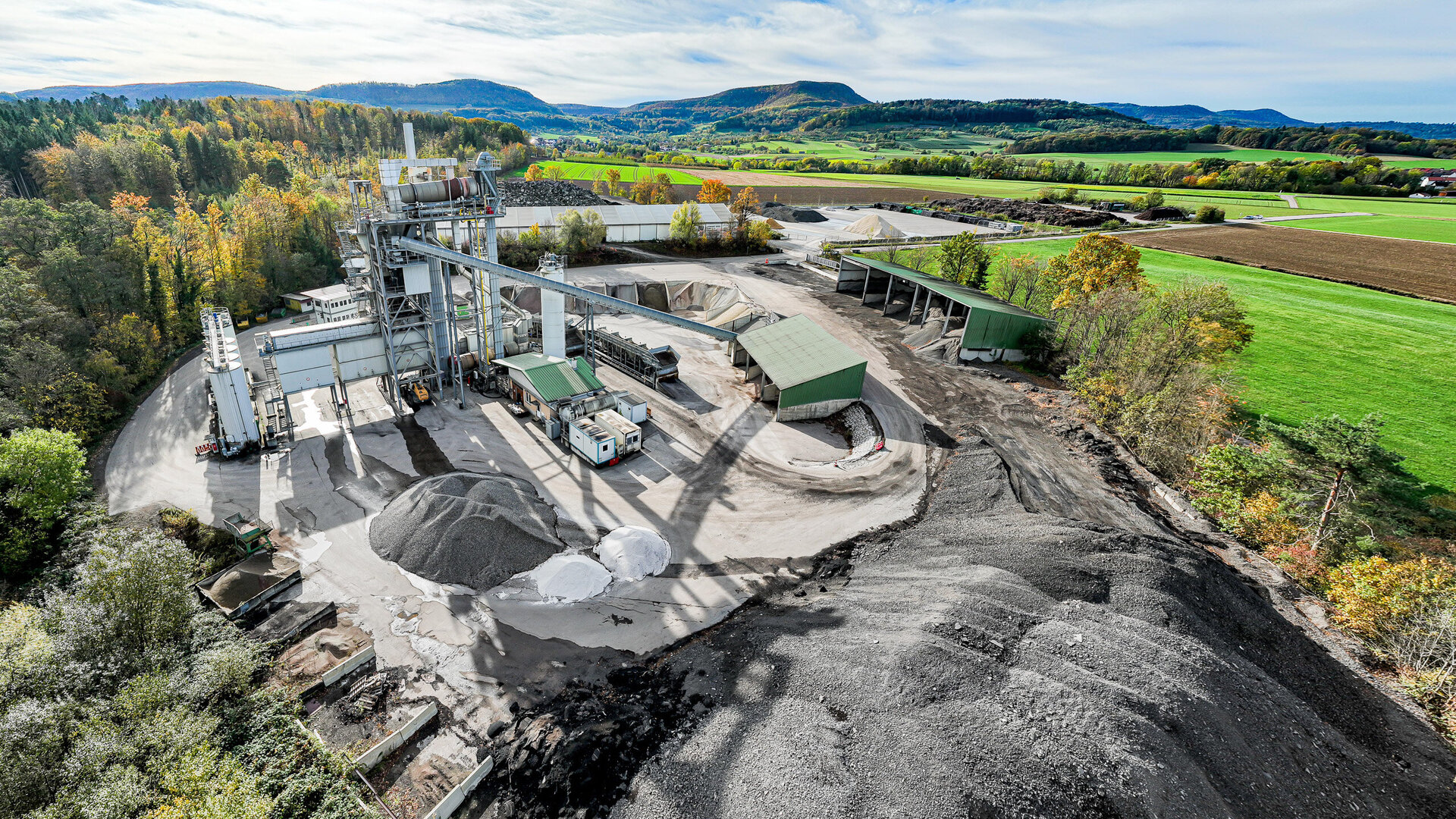 Die Szene zeigt eine industrielle Anlage mit verschiedenen Materialien, darunter Sand und Kies, unter einem klaren Himmel.